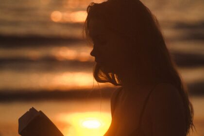 Jonge vrouw leest met ondergaande zon op de achtergrond