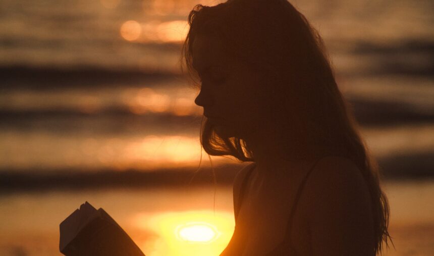 Jonge vrouw leest met ondergaande zon op de achtergrond