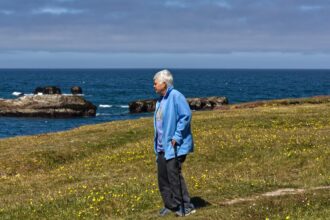 Oudere vrouw met wandelstok staat op het gras naar het water te kijken