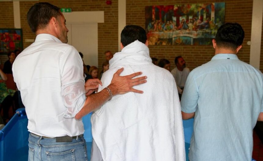 Foto vanaf de achterkant van Jurjen ten Brinke die samen met een andere man een Koerdische man doopt